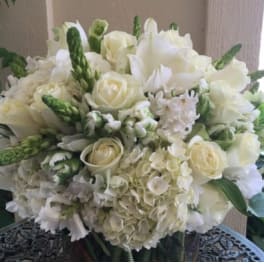Round arrangement of white roses and hydrangeas with green buds in a clear glass vase