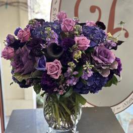 Lavender roses and purple hydrangeas arranged in a clear footed glass vase