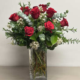 Tall arrangement of red roses with white filler flowers in a clear rectangular glass vase