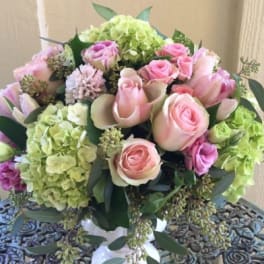 Round arrangement of pink roses and green hydrangeas in a white pedestal vase