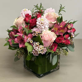 Compact arrangement of pink roses, hyacinths, and mixed blooms in a square glass vase