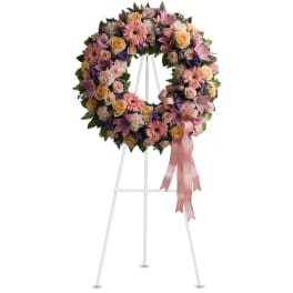 Pastel floral wreath with pink lilies and gerberas on a white standing easel with pink ribbon.