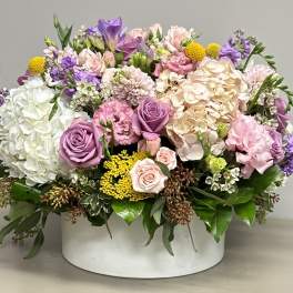 Low round arrangement of pink, lavender, white, and yellow flowers in a white container.