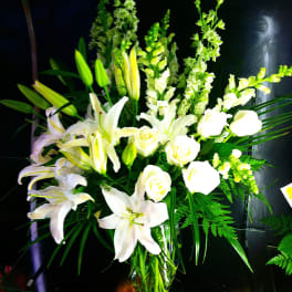 Tall arrangement of white lilies, roses, and snapdragons in a clear glass vase