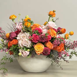 Low centerpiece of bright orange and pink flowers with pale hydrangea in a round white bowl