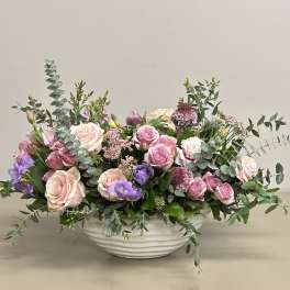 Low centerpiece of pink roses and mixed purple flowers in a white ceramic bowl