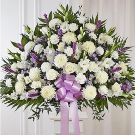 Large white floral spray with a purple ribbon on a stand