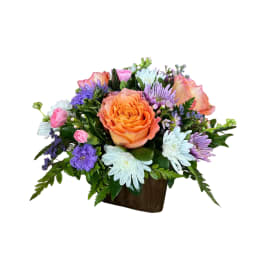 Mixed bouquet with an orange rose and purple and white flowers in a brown container
