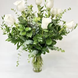 White roses arranged in a clear glass vase with greenery