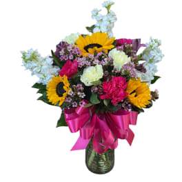 Bright mixed bouquet with sunflowers and pink and white flowers in a glass vase with a hot pink bow