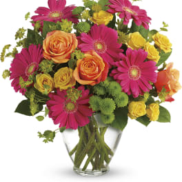 Bouquet of pink gerbera daisies and yellow-orange roses in a clear glass vase