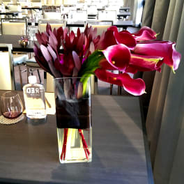 Magenta calla lilies and dark burgundy flowers in a glass vase