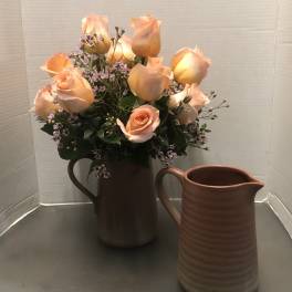Peach roses arranged in a brown pitcher with a matching empty pitcher beside it.