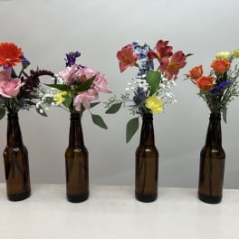 Four small flower arrangements in brown glass bottles on a table