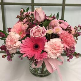 Pink mixed flower bouquet in a clear glass vase with a ribbon