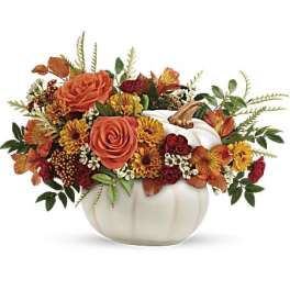 Orange and red floral arrangement in a white pumpkin container