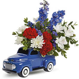 Blue vintage truck figurine holding a red, white, and blue flower arrangement