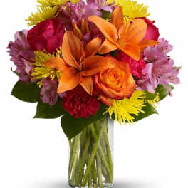 Colorful bouquet of lilies, roses, and daisies in a clear glass vase