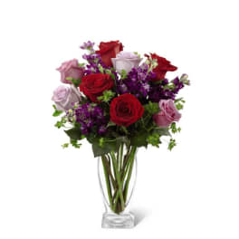 Vase arrangement of red and lavender roses with purple flowers in a clear glass vase.