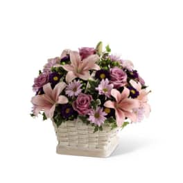 Pink lilies, roses, and purple daisies arranged in a white woven basket
