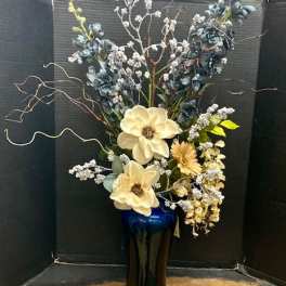 Tall floral arrangement in a blue vase with cream blooms and blue accents