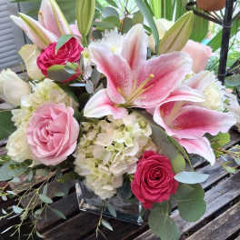 Pink lilies and roses arranged in a square glass vase