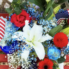 Red, white, and blue floral arrangement with lilies, roses, and small flags