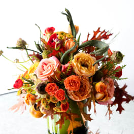Autumn bouquet of orange and pink roses with fall leaves in a glass vase