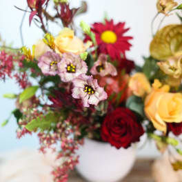 Mixed bouquet with roses and daisy-like blooms in a white vase