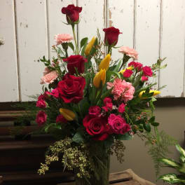 Tall bouquet of red roses, pink carnations, and yellow tulips in a glass vase