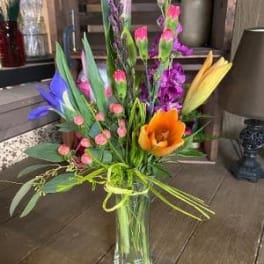 Tall mixed bouquet in a clear glass vase with orange, purple, pink, and yellow blooms
