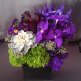 Purple orchids and calla lilies in a black square vase