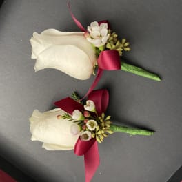Two white rose boutonnieres with burgundy ribbon accents