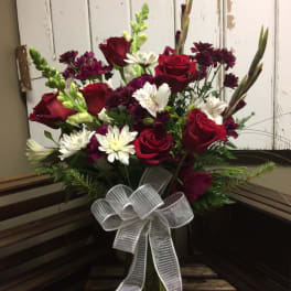 Bouquet of red roses, white daisies, and purple flowers in a glass vase with a white bow