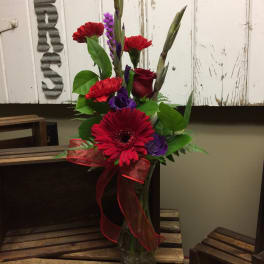 Red and purple flower arrangement in a glass vase with a ribbon