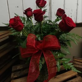 Red roses arranged in a glass vase with a large red ribbon.