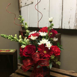 Red and white mixed flower arrangement in a dark vase with a red ribbon