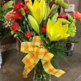 Bouquet of yellow lilies and red flowers in a glass vase with a plaid bow