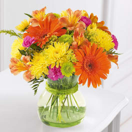 Bright mixed bouquet of orange, yellow, and pink flowers in a glass vase