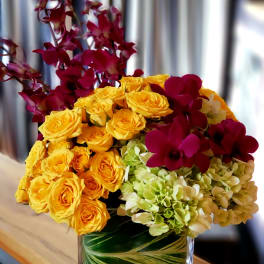 Bouquet of yellow roses, green hydrangeas, and burgundy orchids in a glass vase