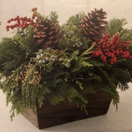Holiday centerpiece with pinecones, evergreen branches, and red berries in a wooden container
