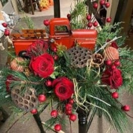 Red roses and holiday greenery arranged with a small orange toy truck