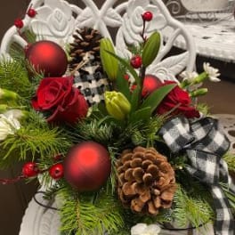 Holiday floral arrangement with red roses, pinecones, and ornaments in a white chair