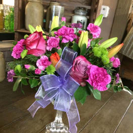 Pink and purple flower arrangement in a clear vase with a lavender ribbon
