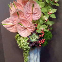 Pink anthuriums and green orchids in a tall blue vase