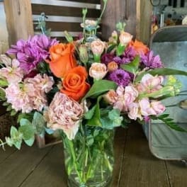 Mixed bouquet of orange, pink, and purple flowers in a glass vase