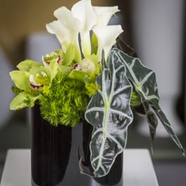 White calla lilies and green flowers in a dark glass vase