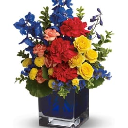 Bright mixed bouquet in a square glass vase with blue, red, and yellow flowers