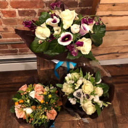Three mixed flower bouquets with roses and calla lilies on a wooden floor