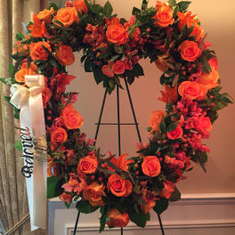 Orange rose wreath on a black stand with a white ribbon